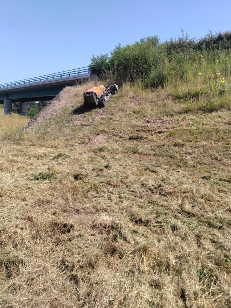 Robot broyeur télécommandé fauchant le talus en pente d'un bord de route à Dax, sous un pont